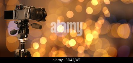 Professionelle Kamera vor verschwommenem Hintergrund mit Bokeh-Lichtern. Bannerdesign Stockfoto