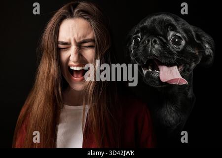 Verängstigte Frau, die an Zynophobie leidet, schwarzer Hintergrund. Pathologische Angst bei Hunden Stockfoto