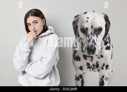 Verängstigte Frau, die an Zynophobie leidet, grauer Hintergrund. Pathologische Angst bei Hunden Stockfoto