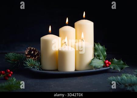 Brennende Kerzen mit stechpalmenblättern, roten Beeren und Tannenzweigen schaffen eine warme Weihnachtsatmosphäre. Stockfoto