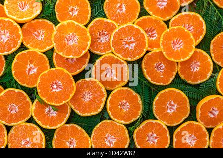 Frische Orangen und Mandarinen auf einem Markt. Ganze Orangen sind hoch gestapelt, während geschnittene Orangen auf einem Bett aus grünen Blättern angeordnet sind. Stockfoto