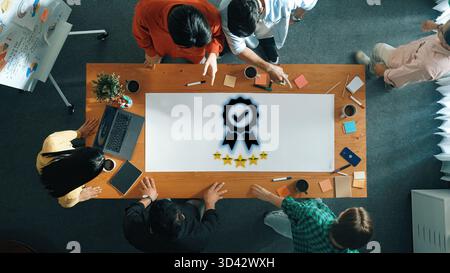 Ein vielseitiges Geschäftsteam nimmt an einem kreativen Meeting rund um einen großen Holztisch Teil und stellt in einer modernen Büroumgebung die Auszeichnung zum Ausdruck. Trope Stockfoto