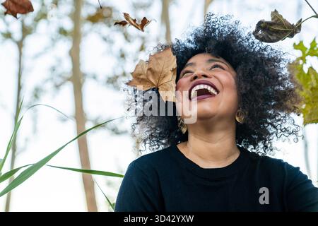 Glückliche junge Frau genießt herbstliche Blätter im Freien und drückt Freude aus Stockfoto