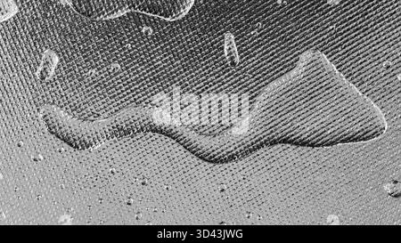Makroaufnahme mit Wassertropfen auf Folie oder strukturiertem Metallic. Monochromatisches Silber mit klarem Rautengitter oder gewebter Netzstruktur Stockfoto