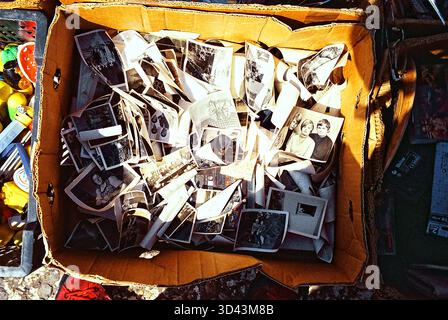 Box gefüllt mit privaten Schwarzweißfotos auf einem sonnigen Flohmarkt, nostalgischer analoger Atmosphäre und Vintage-Texturen. Stockfoto