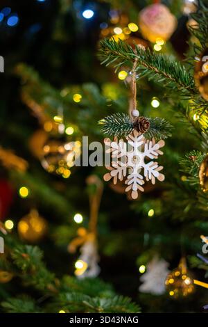 Sterne und goldene Weihnachtskugeln hängen als Dekoration an einem Weihnachtsbaum mit goldenen Lichtern. Dekoriere den Weihnachtsbaum mit einer Holzschneeflocke Stockfoto