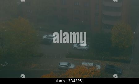 Herbststraße von oben mit bunten gelben Bäumen und geparkten Autos am nebeligen Morgen Stockfoto