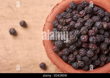 Makroaufnahme schwarzer Pfefferkörner in rustikaler Terrakotta-Schüssel auf Holzoberfläche, Soft Focus und Kopierraum für Text, kulinarische Gewürze und rustikale Küche Stockfoto