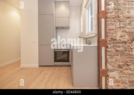 Panoramablick auf eine kleine, moderne Küche mit weißen Melaminschränken und einer Quarzarbeitsfläche, optisch in die Frühstücksecke integriert Stockfoto