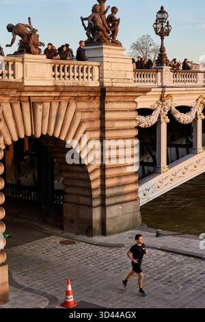Der Läufer genießt einen Jog bei Sonnenuntergang in der Nähe der historischen Brücke Alexandre III in Paris mit lebhaften Zuschauern über Paris, Frankreich Stockfoto