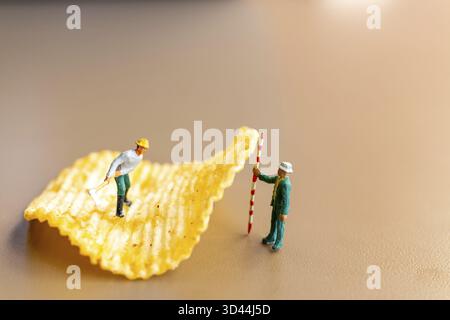 Miniaturmenschen: Arbeiter arbeiten mit Kartoffelchips Stockfoto