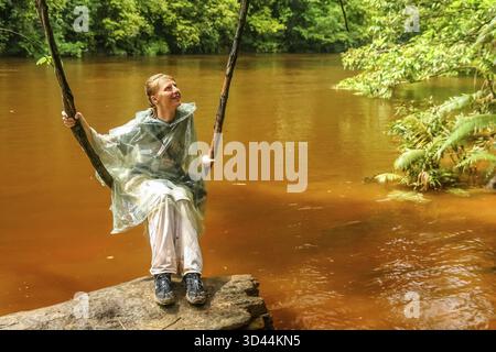 Frau sitzt auf einem natürlichen Schwung über Fluss im malaysischen Dschungel im Nationalpark Taman Neggara Stockfoto