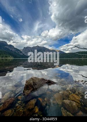 Gebirgskette und klarer blauer Himmel spiegeln sich im ruhigen klaren Wasser eines Bergsees wider Stockfoto