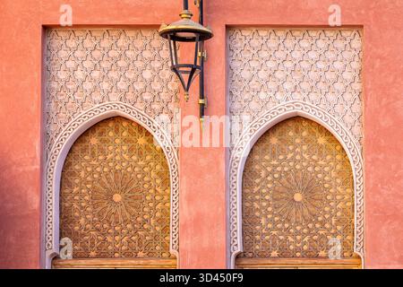 Marokkanische Architektur in Marrakesch Medina mit geschnitzten Bogentüren, geometrischen islamischen Mustern und einer Laterne unter kunstvollen Holzdetails. Stockfoto