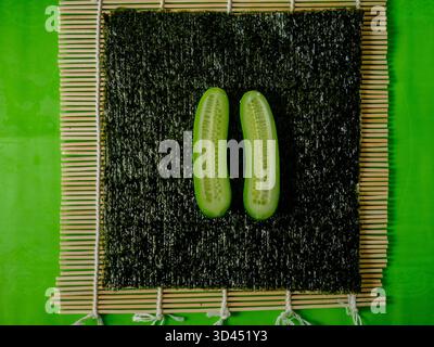 Draufsicht von zwei frischen Gurkenhälften auf Nori-Blatt und Bambusmatte, Zutat für Sushi-Zubereitung Foto für Küchen- und Kochkünstler. Hohe Qual Stockfoto