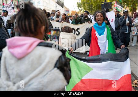 London, Großbritannien. November 2025. Eine Frau hält eine sudanesische Flagge, während sie während der Kundgebung von der Tochter auf Video aufgenommen wird. Demonstranten marschierten in London, um Solidarität mit dem sudanesischen Volk zu zeigen und für ein Ende der britischen Waffenverkäufe an die VAE zu plädieren, die laut Aktivisten Gräueltaten der RSF-Miliz im ganzen Land ermöglichen. Quelle: SOPA Images Limited/Alamy Live News Stockfoto