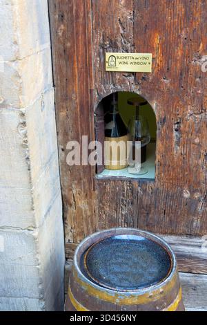 Nahaufnahme einer traditionellen Buchetta del Vino in Florenz, Italien - ein altes Weinfenster mit einer Flasche und einem Glas in einer rustikalen Holzwand. Stockfoto
