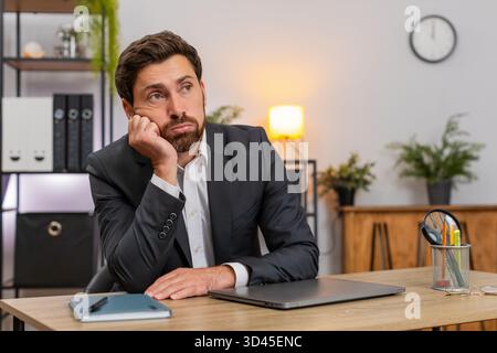 Ein Geschäftsmann mittleren Alters im Home Office schließt den Laptop schnell und ärgert sich über langweilige Aufgaben. Freelancer Guy am Tisch reibt Augen dehnt sich macht kurze Pause und kehrt dann wieder zur Arbeit zurück. Stockfoto