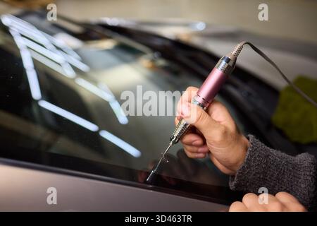 Der Glasreparaturprozess, eine detaillierte Aufnahme von Harzfüllungsfehlern an der Windschutzscheibe, konzentriert sich auf die sorgfältige Reparatur von sternförmigen Spänen an der Windschutzscheibe des Autos Stockfoto
