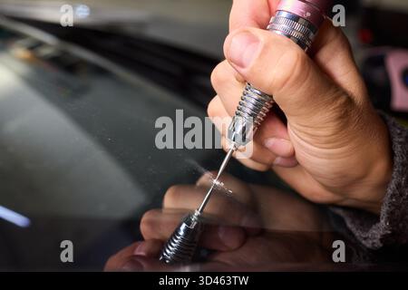 Der Glasreparaturprozess, eine detaillierte Aufnahme von Harzfüllungsfehlern an der Windschutzscheibe, konzentriert sich auf die sorgfältige Reparatur von sternförmigen Spänen an der Windschutzscheibe des Autos Stockfoto