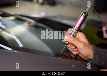 Der Glasreparaturprozess, eine detaillierte Aufnahme von Harzfüllungsfehlern an der Windschutzscheibe, konzentriert sich auf die sorgfältige Reparatur von sternförmigen Spänen an der Windschutzscheibe des Autos Stockfoto