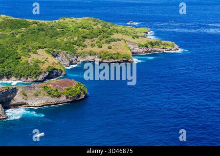 Aus der Vogelperspektive auf die zerklüftete grüne Küste und das tiefblaue Meer von Nusa Penida, Bali Stockfoto