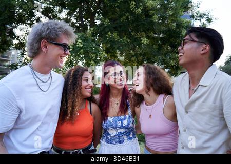 Multikulturelle Gruppe von Freunden, die sich gegenseitig lächeln sehen, während sie sich im Kreis draußen umarmen. Stockfoto