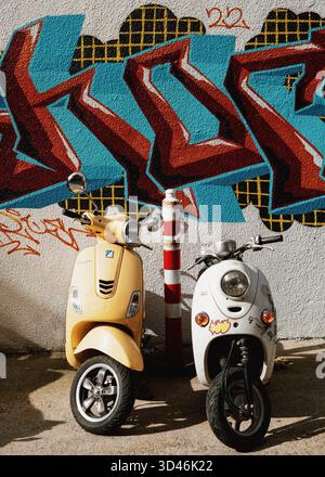 Sammlung von gelben, roten und weißen Motorrollern im Vintage-Stil, die auf der städtischen Straße vor bunten Wänden geparkt sind und Street Art of Georgia zeigen Stockfoto