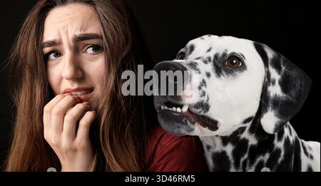 Verängstigte Frau, die an Zynophobie leidet, schwarzer Hintergrund. Pathologische Angst bei Hunden Stockfoto