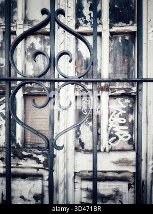 Nahaufnahme von schmiedeeisernen Gittern vor einer verwitterten Holztür mit abblätternder Farbe und Graffiti Stockfoto