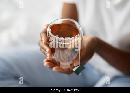Schwarze Frau im Pyjama genießt Kräutertee im Bett während eines ruhigen Morgenmoments Stockfoto