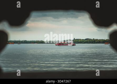 Ein detaillierter Blick auf ein rotes Passagierboot, das über einen ruhigen See in Peking, China, unter einem bewölkten Himmel fährt, mit subtilen Details. Stockfoto