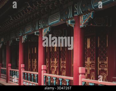 Dieses Bild fokussiert auf architektonische Details in Peking, China, und fängt die leuchtenden roten Säulen und exquisit verzierten Türen eines traditionellen Gebäudes ein Stockfoto