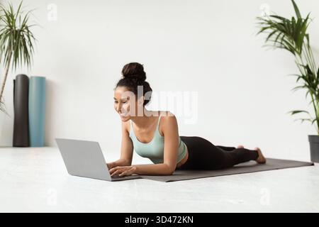 Junge Frau genießt Online-Yoga-Tutorials, während sie sich zu Hause auf einer Fitnessmatte entspannt Stockfoto