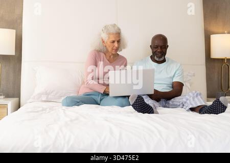 Das Bett im Schlafzimmer mit silbernem Laptop und weißen Kissen ist ein vielseitiges Seniorenpaar Stockfoto