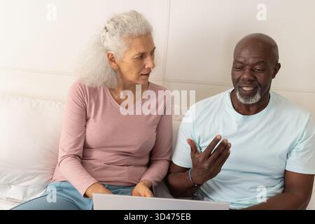 Seniorenpaar teilt sich einen silbernen Laptop im Wohnzimmer und prüft Dokumente zusammen Stockfoto