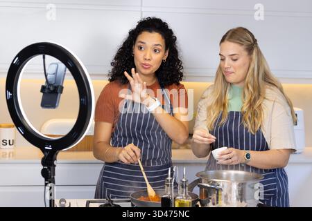 Kochen Sie verschiedene weibliche Freunde, die Sauce und Würze in moderner Küche mit Ringlicht zubereiten Stockfoto