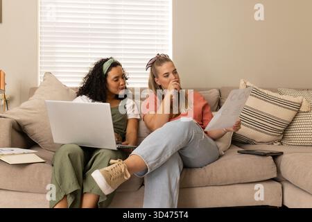 Zusammenarbeit mit verschiedenen weiblichen Freunden, die Diagramme auf Sofa im Wohnzimmer studieren, mit silbernem Laptop Stockfoto