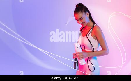 Sportlerin posiert mit Fitness Bottle und springendem Seil vor Neonhintergrund Stockfoto