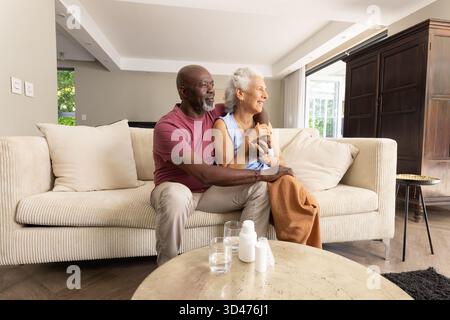 Verschiedene Paare sitzen auf Cordsofa im Wohnzimmer, mit Pillen-Flaschen und Wassergläsern Stockfoto