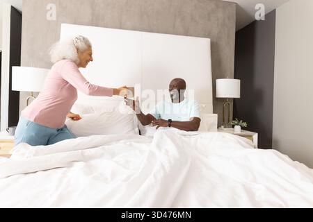 Seniorenpaar teilen sich Morgenkaffee im Bett im modernen Schlafzimmer mit Keramikbecher und weißer Bettwäsche Stockfoto