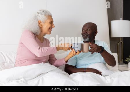 Graue und beigefarbene Tassen verschiedene Seniorenpaare sitzen zu Hause im Bett, mit weißer Bettwäsche Stockfoto