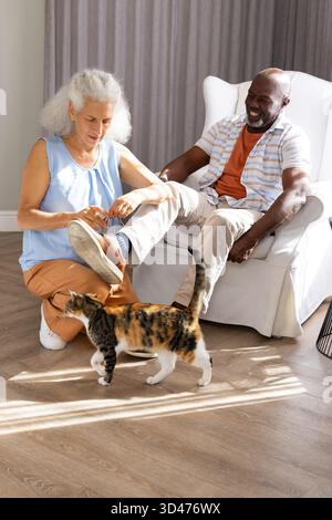Knien verschiedene Seniorenpaare, die Schnürsenkel auf Holzboden im Wohnzimmer binden, mit Calico Katze Stockfoto