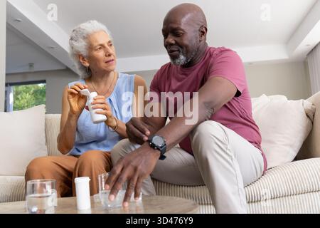Abgeben von Pillen Seniorenpaar auf Sofa im Wohnzimmer, mit Pillen-Flaschen und Wassergläsern Stockfoto