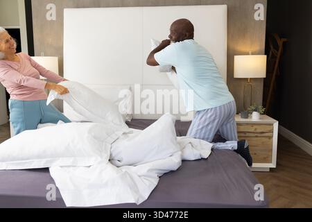 Verschiedene Seniorenpaare haben Kissenkampf im Hauptschlafzimmer, mit weißen Kissen und Holzleiter Stockfoto