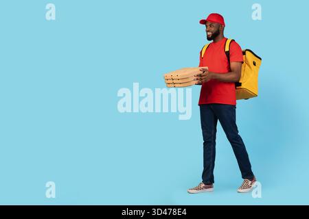 Junger Lächelnder Black Courier Guy Trägt Thermal Backpack Walking Mit Pizzakisten Stockfoto