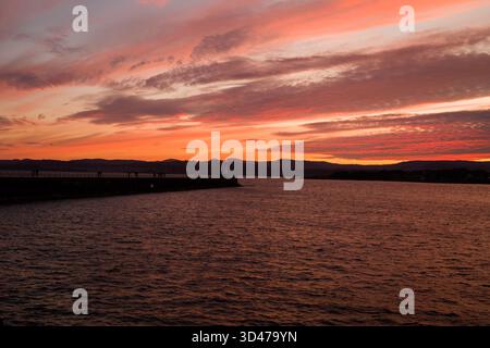 Ein lebhafter Sonnenuntergang über der Pazifikküste, der Himmel ist mit leuchtenden Farben gesättigt, der Horizont ist von fernen Hügeln geprägt. Stockfoto