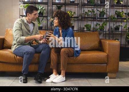 In der modernen Lounge lehnten sich verschiedene Freunde auf der Ledercouch und hielten dunkle Kaffeetassen in der Hand Stockfoto