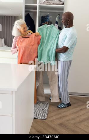 Sie zeigen verschiedene Seniorenpaare, die Hemden im Ankleidebereich aussuchen, mit Korallenbluse und grünem Hemd Stockfoto