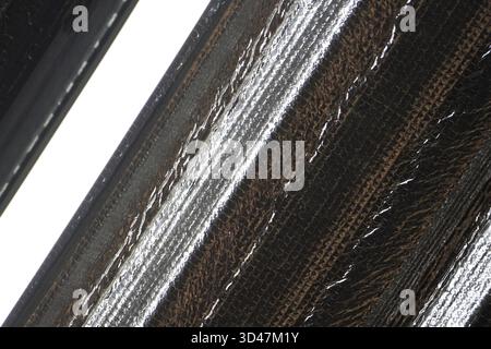 Details aus modernem Verbundmaterial mit genähtem diagonalem Muster. Dunkler abstrakter Hintergrund mit gewebter Textur mit starkem Metallic-Glanz Stockfoto
